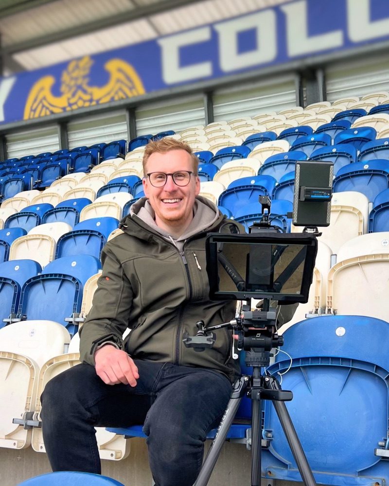 Sam Martin, founder of The Sequence, smiling in the stadium seats with his camera