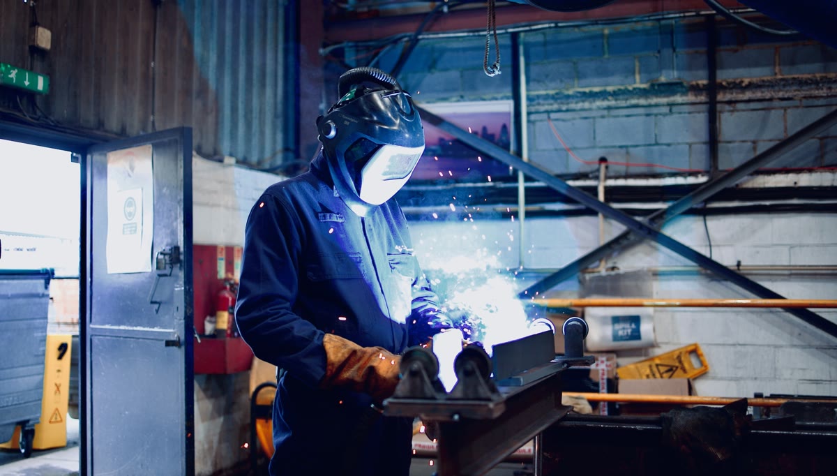 Apex Steel Structures welder fabricating a steel section in the workshop, sparks flying