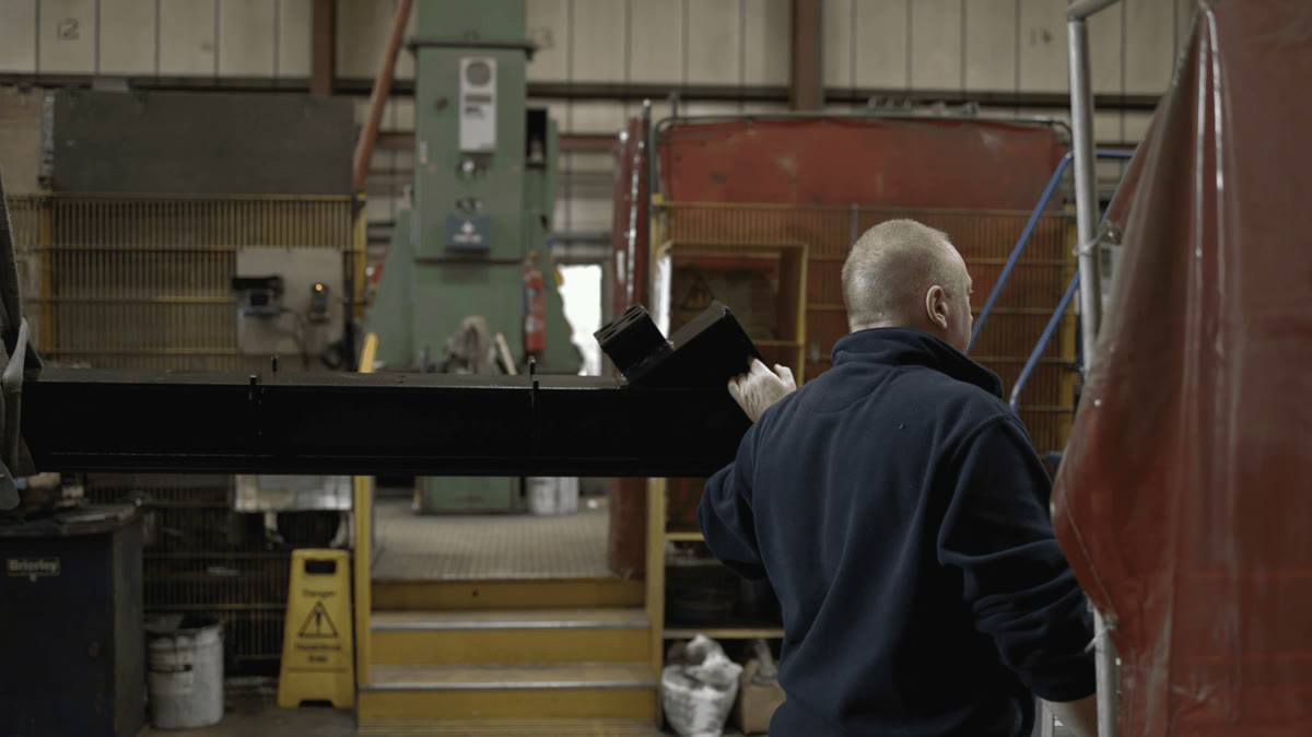 An Apex fabricator working a large welded steel beam in the workshop