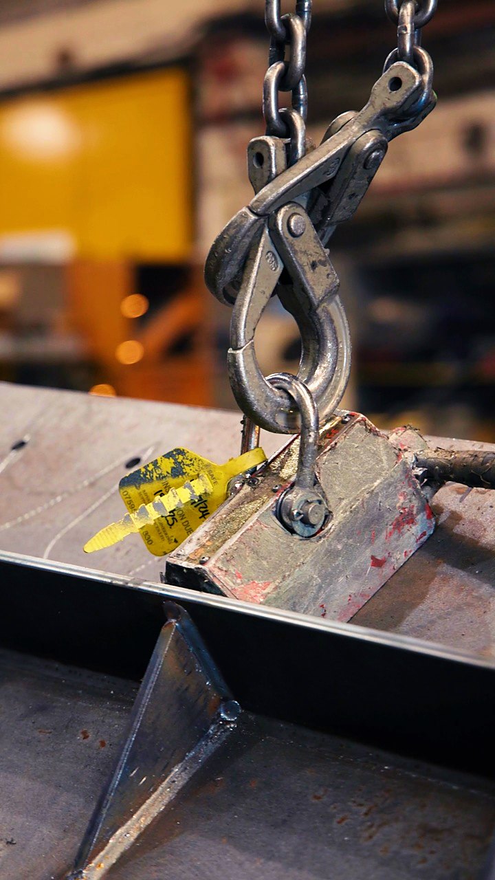 A crane hook and magnet lifting a steel plate in the workshop