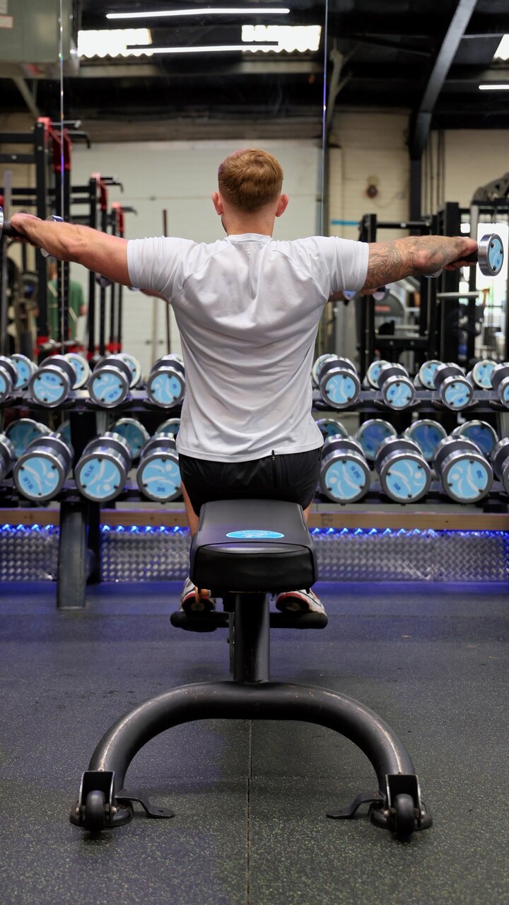 A member on the bench in front of the dumbbell rack
