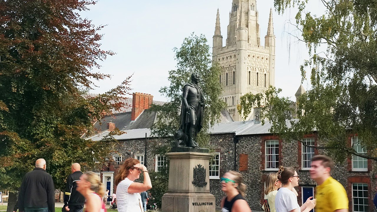 Runners passing the statue with Norwich Cathedral spire behind