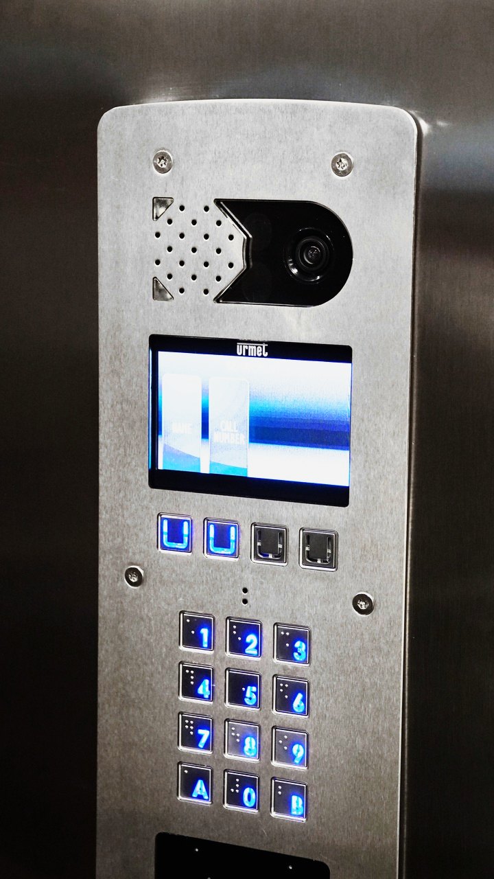 A close up of an Urmet stainless steel door entry panel with a lit keypad