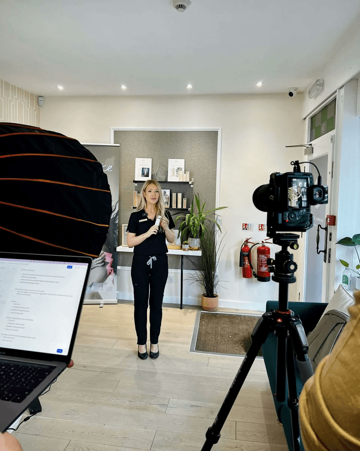 Sasha presenting to camera in her skin and laser clinic during a content shoot, with softbox lighting and a camera on a tripod