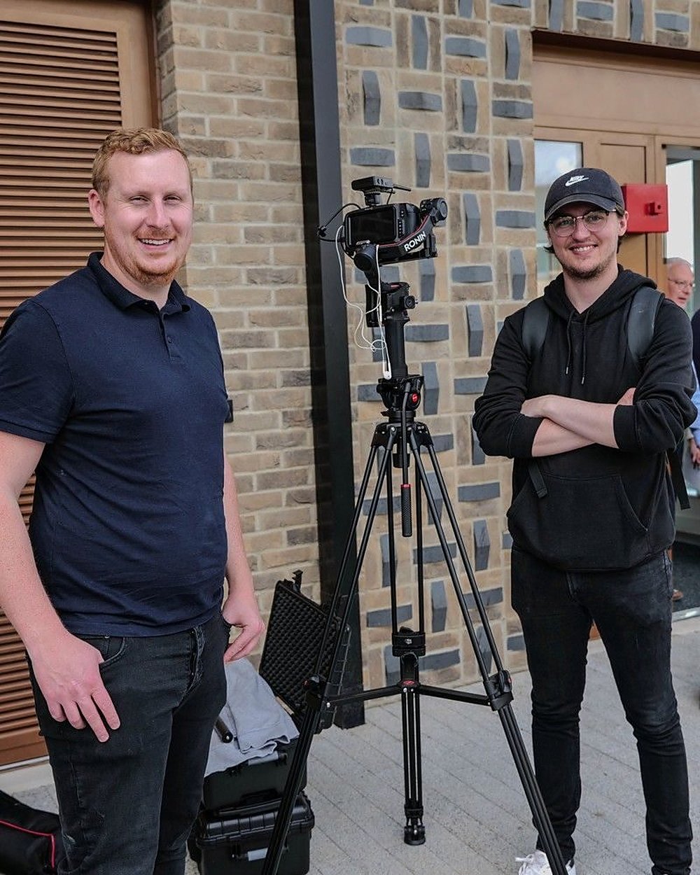 Sam and a colleague either side of a camera on a tripod, setting up a shoot outside a venue