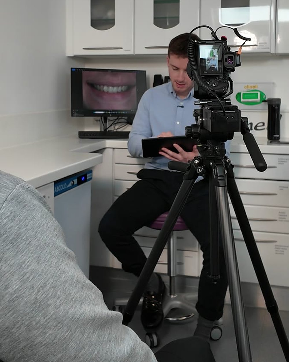 A dentist reading a script on a tablet before an interview, with a camera on a tripod in the foreground