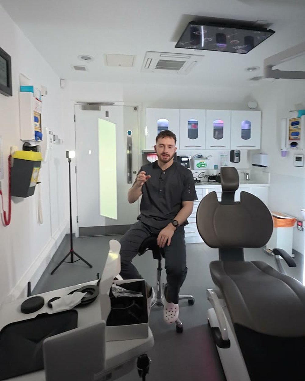 Interview setup in a dental surgery, a dentist seated on a stool talking to camera with an LED light beside the camera