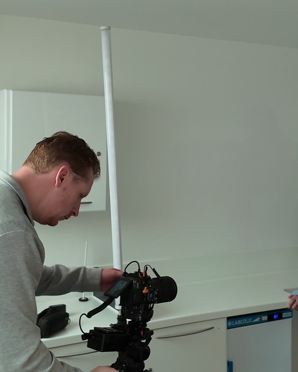 Sam leaning over a cinema camera on a tripod, adjusting it in a bright room