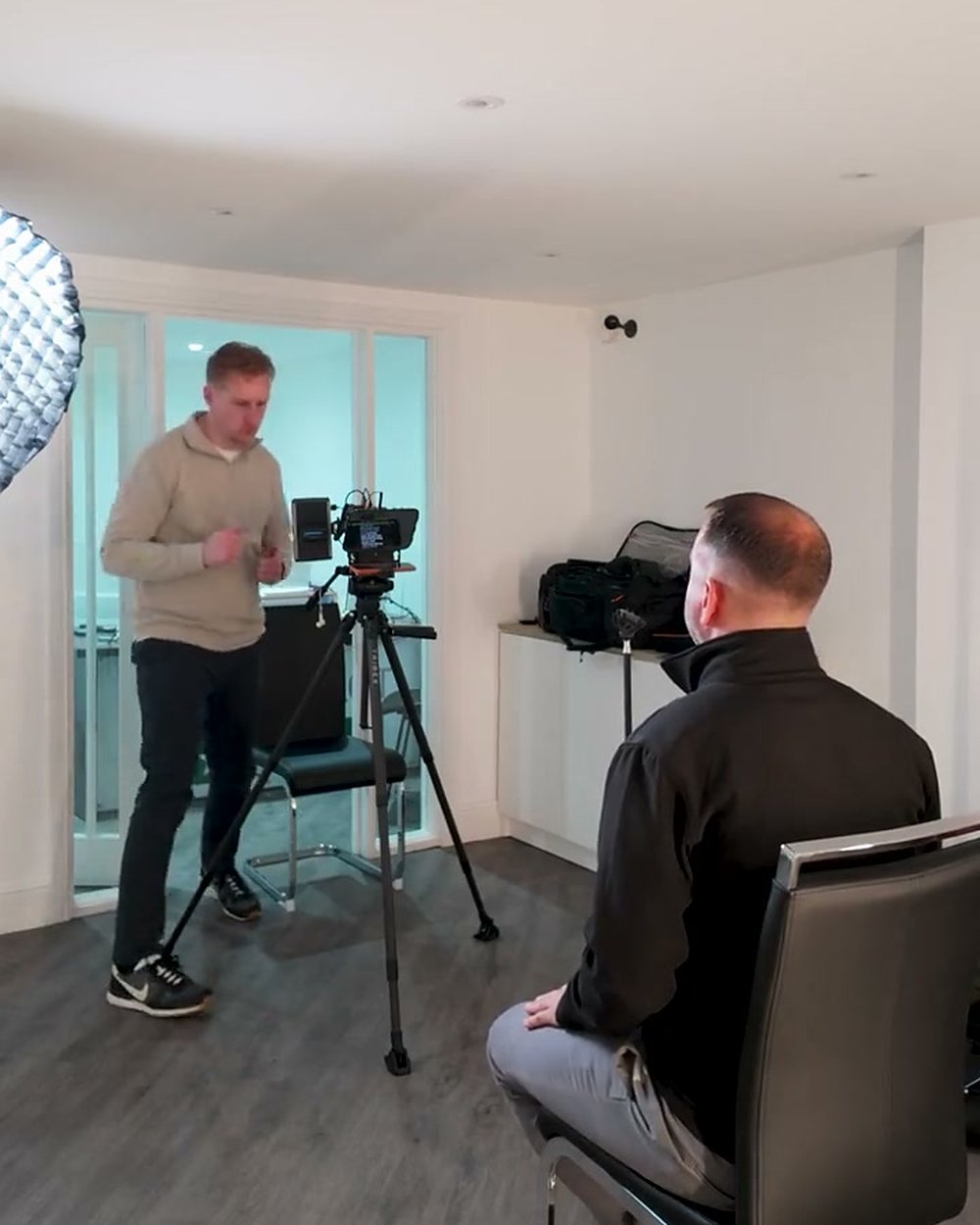 Sam beside the camera on a tripod talking the interviewee through the questions