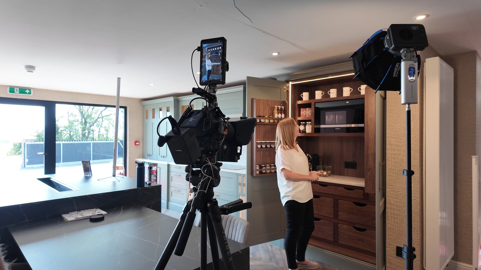 Camera and monitor on a tripod with a light, a presenter at a showroom kitchen island