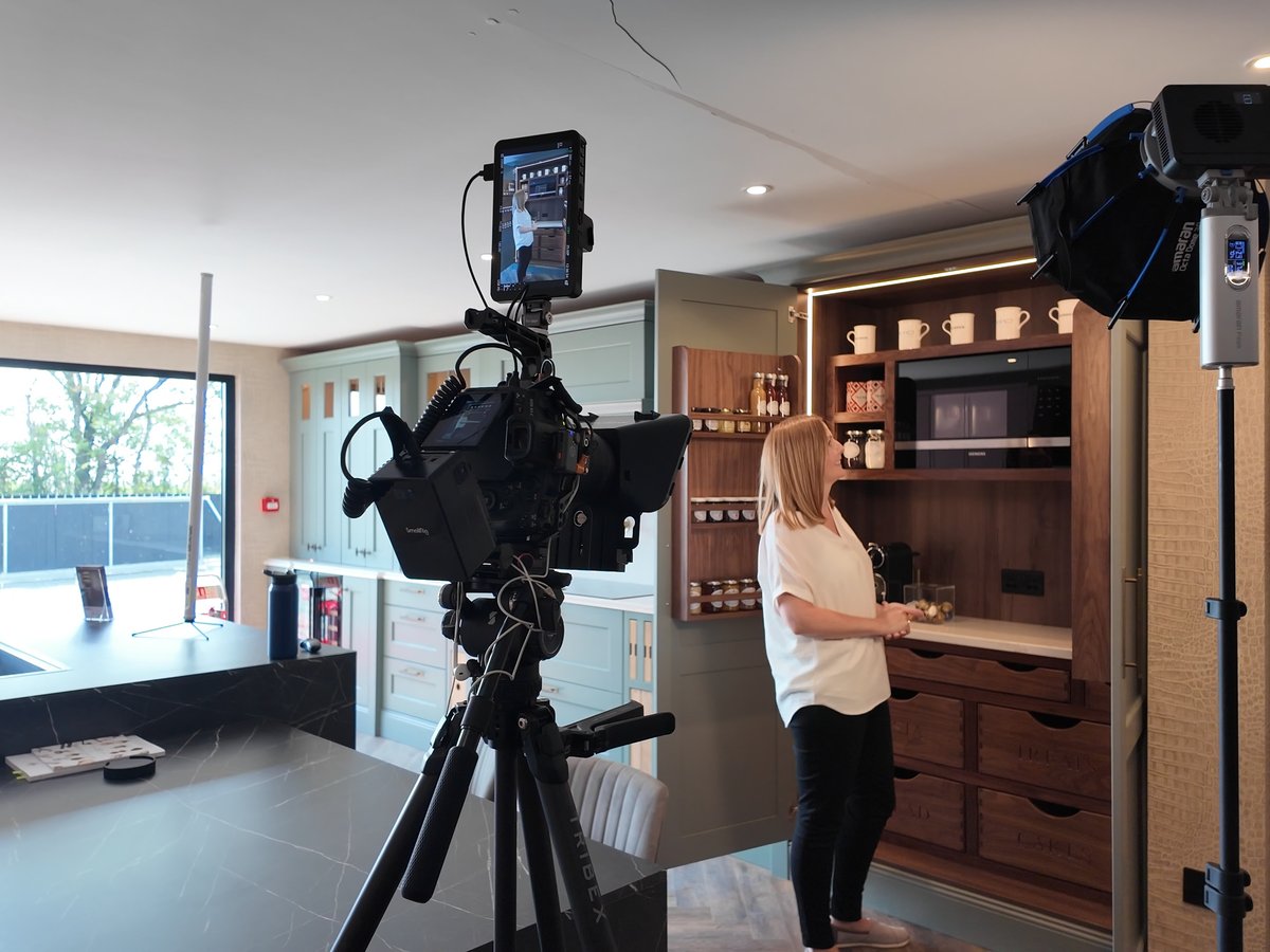 Camera and monitor on a tripod with a light, the presenter at a kitchen island in a showroom