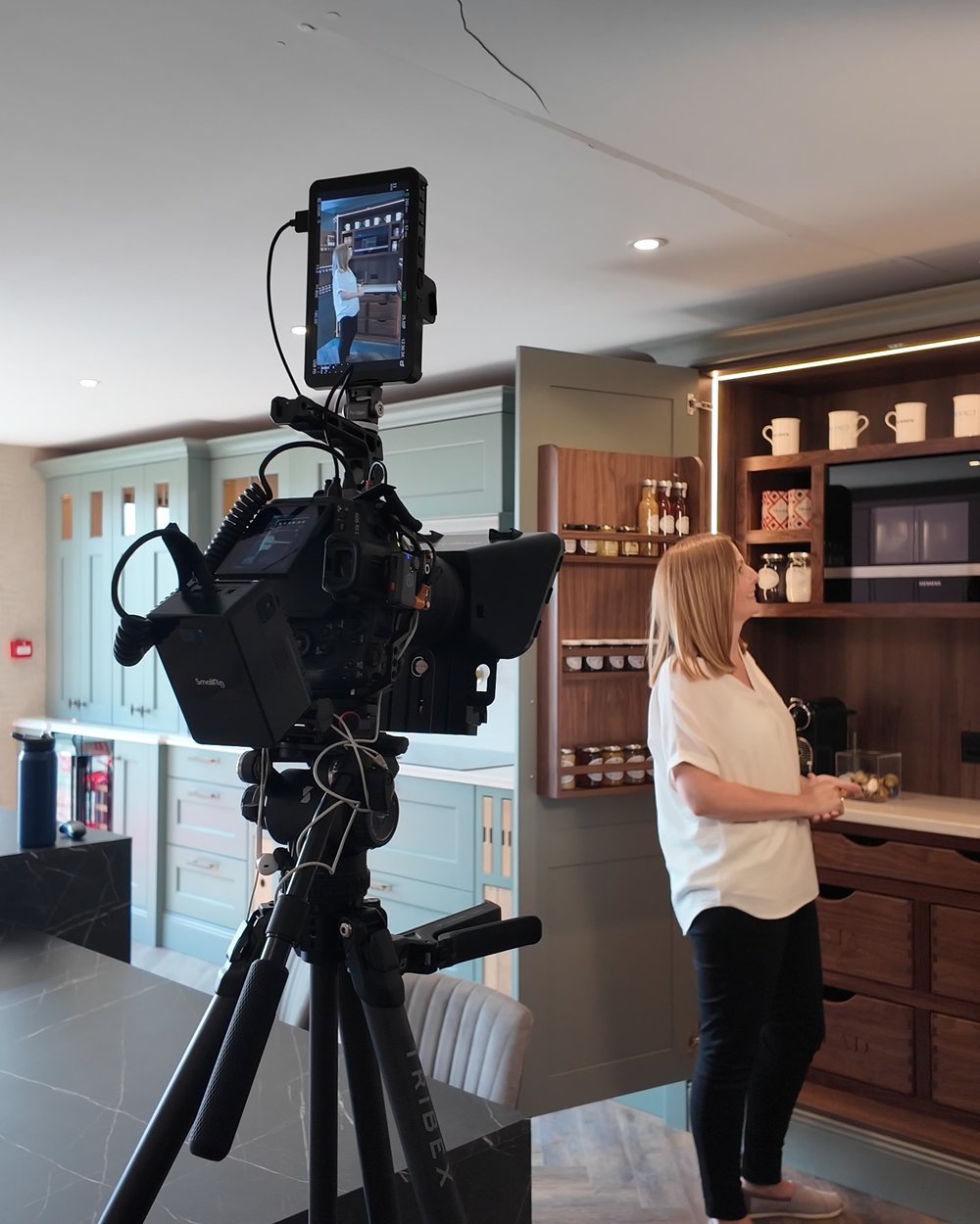 Our camera rig on a tripod in a kitchen showroom, filming a presenter at the units