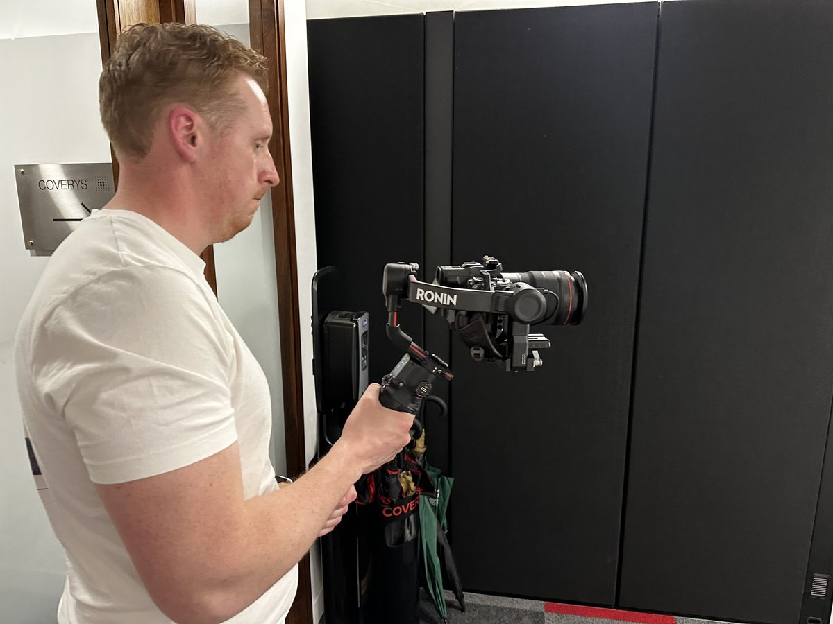 Sam holding a camera on a handheld gimbal, shooting a moving behind the scenes shot in an office
