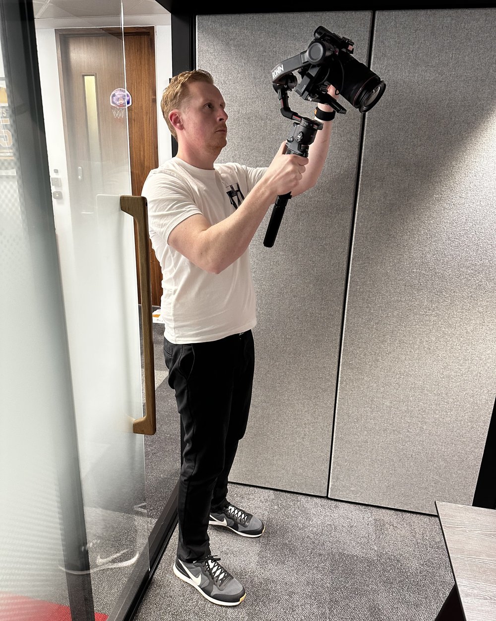 Sam holding a gimbal camera high in an office corridor to capture a moving shot