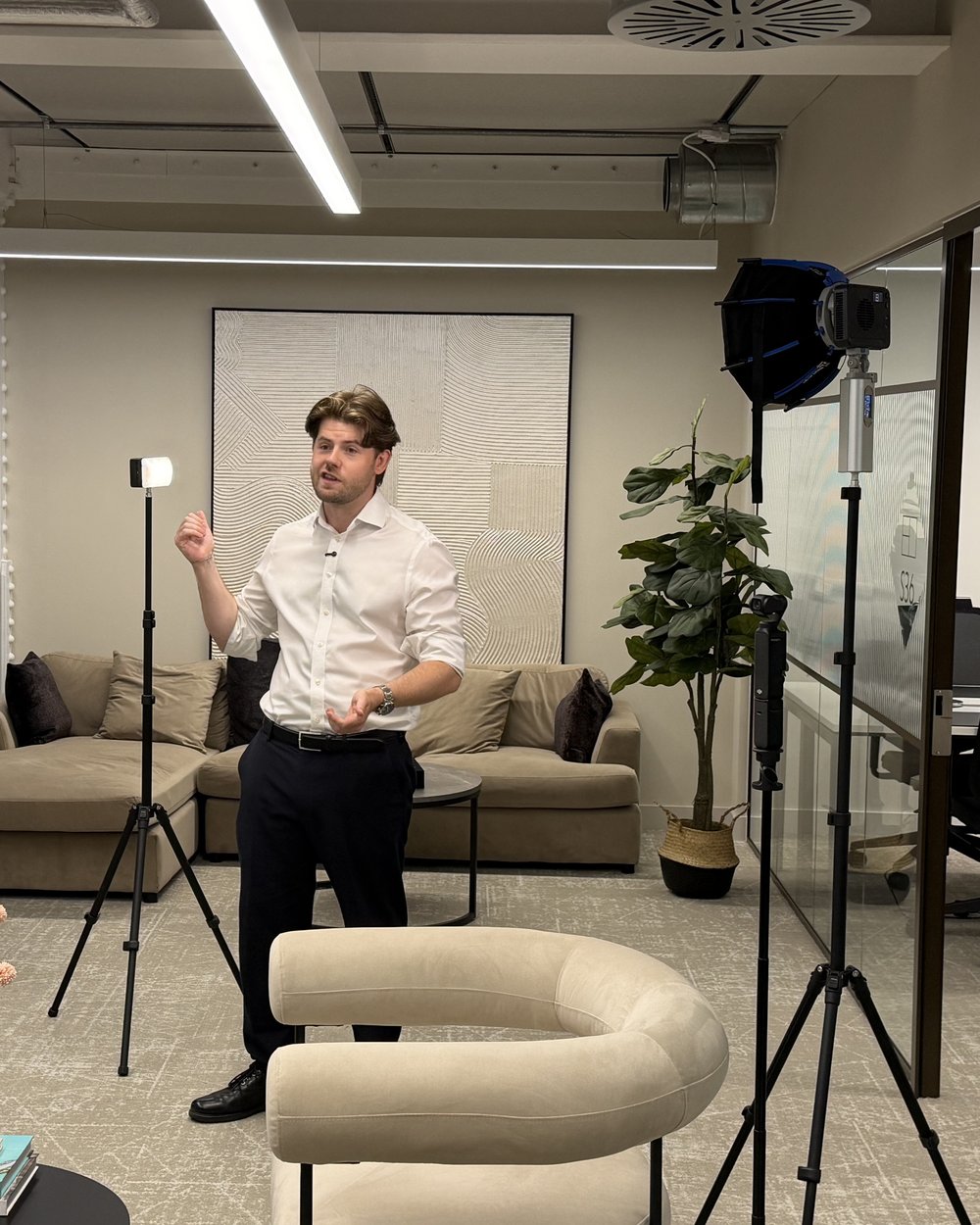 A presenter rehearses on a lit set in an office lounge during a shoot