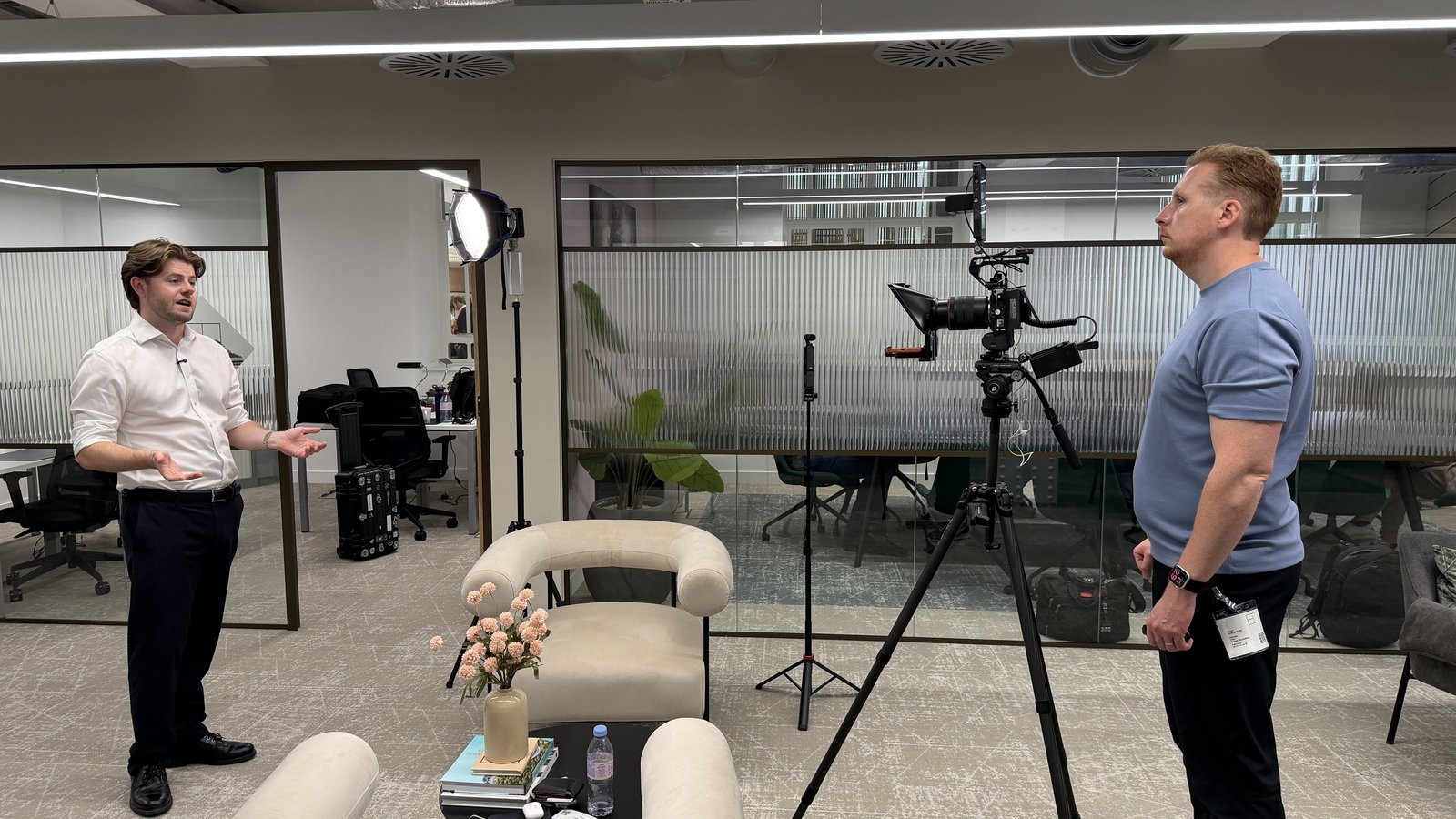 Sam talking an interviewee through the shot beside a camera on a tripod in an office lounge