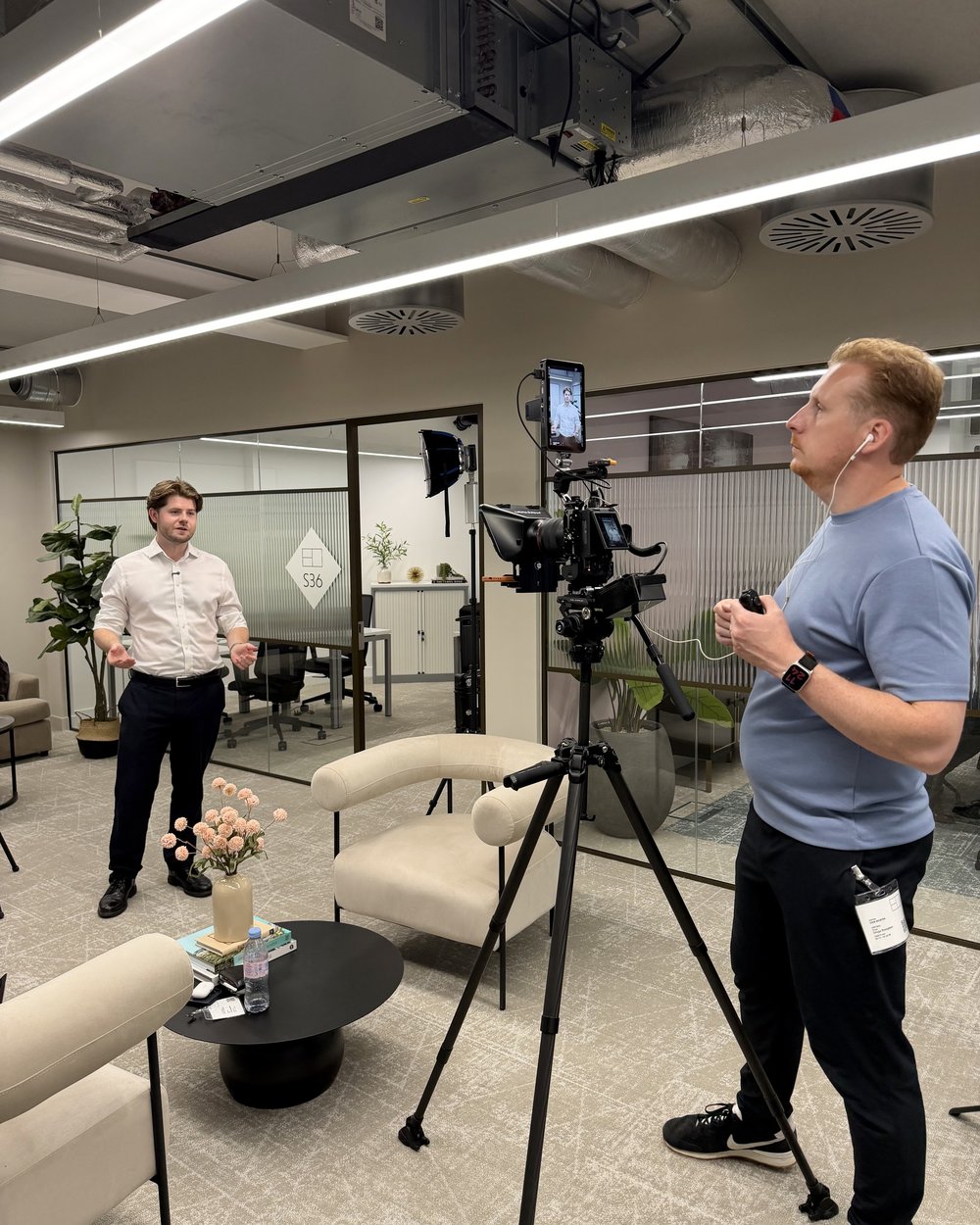 Sam talking an interviewee through a take in a lit lounge set, camera remote in hand