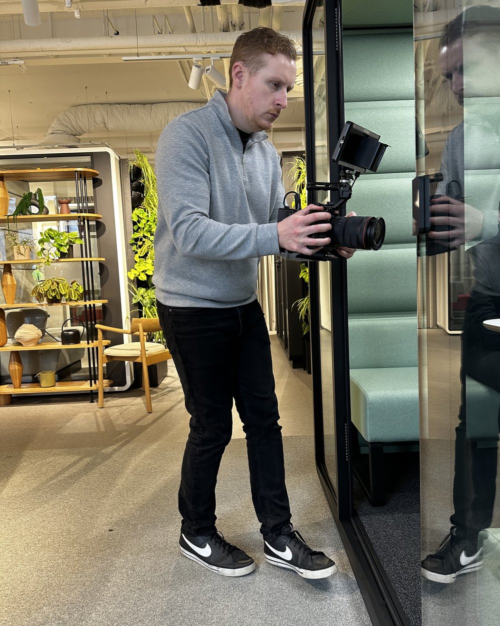 Sam walking with a handheld camera rig past a glass meeting pod in a furniture showroom