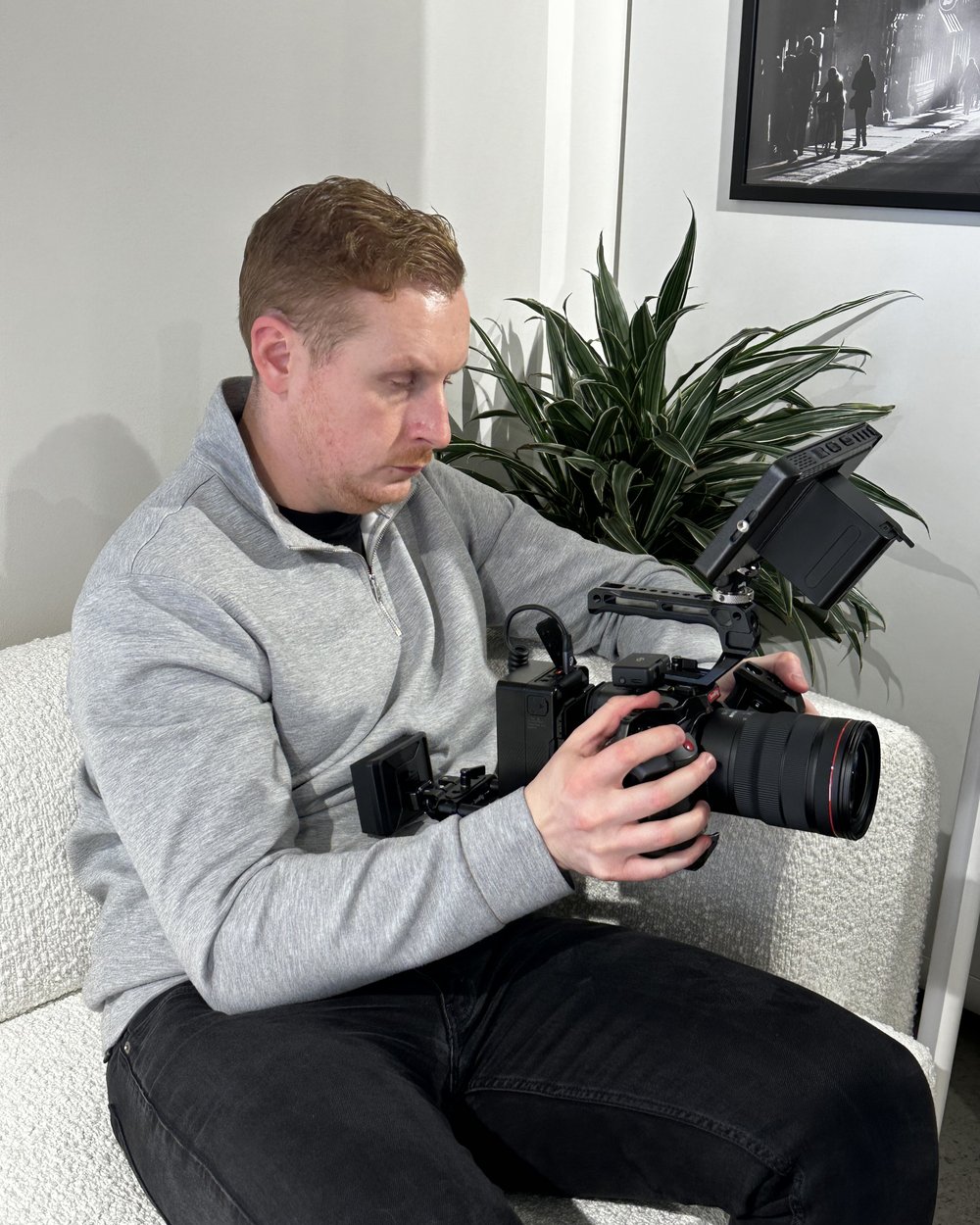 Sam seated on a sofa framing a shot with a camera, shotgun mic and monitor