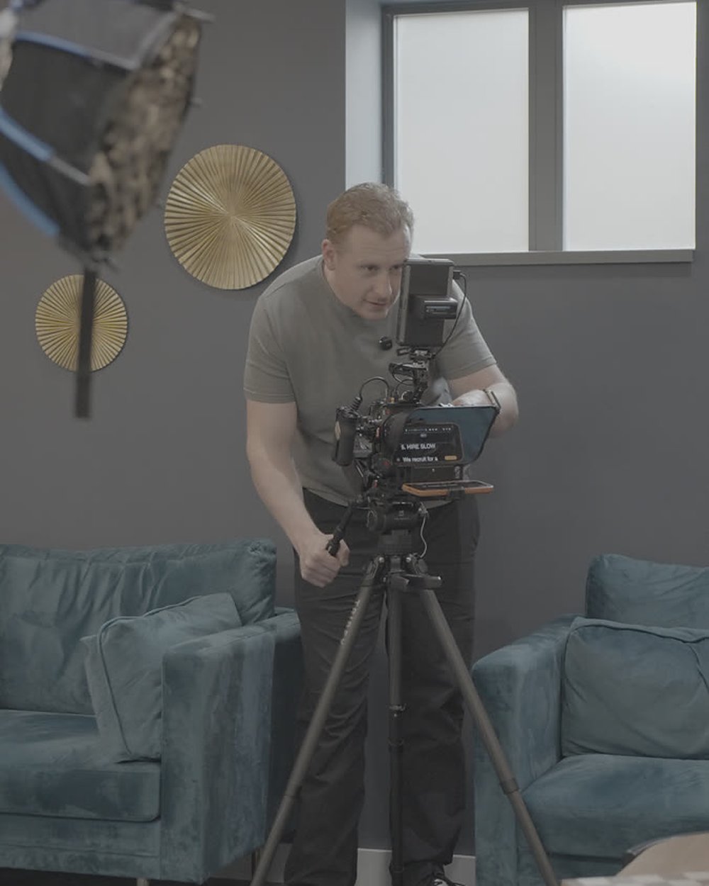 Sam adjusting the camera and teleprompter on a tripod in an interview set before a leadership video