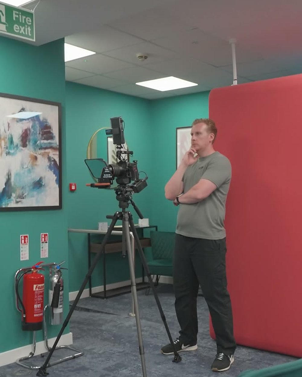 Sam beside a camera and teleprompter on a tripod on the set for Liz Flavell's brand video