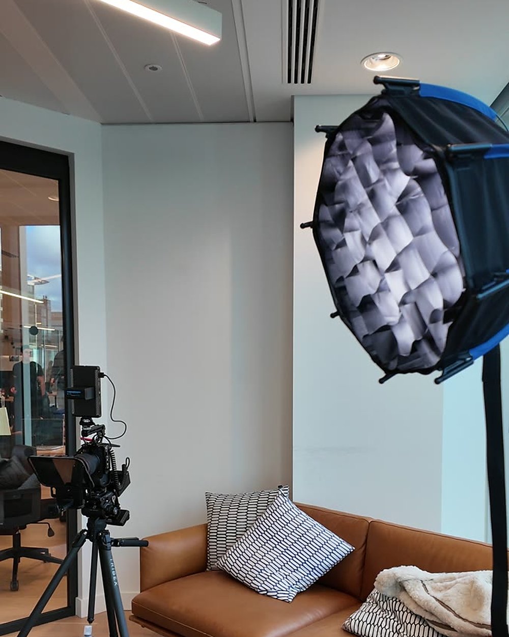 Softbox and camera on a tripod set up beside a leather sofa for a customer interview