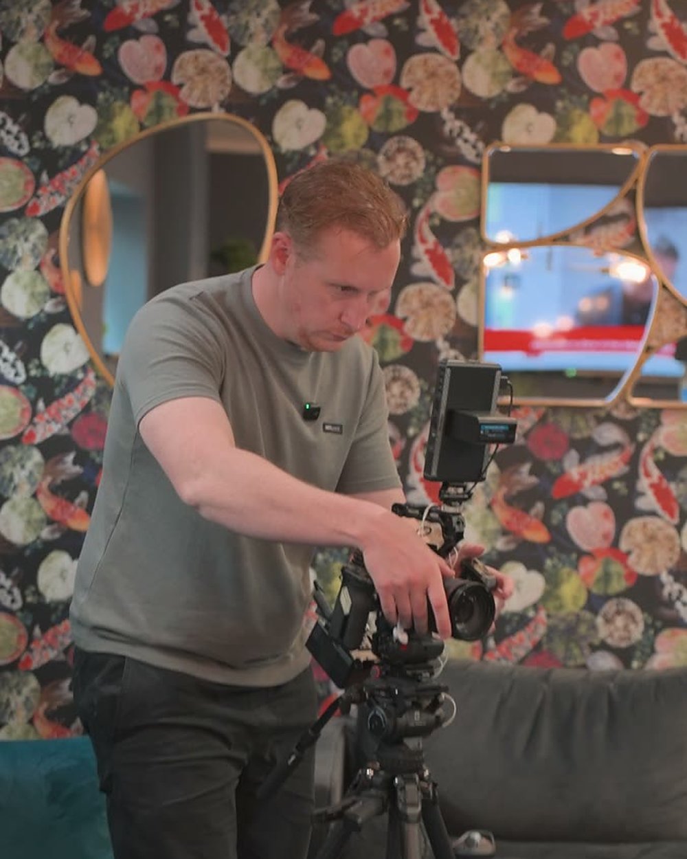 Sam operating the camera on a tripod in front of a floral wallpaper wall on a coach's shoot