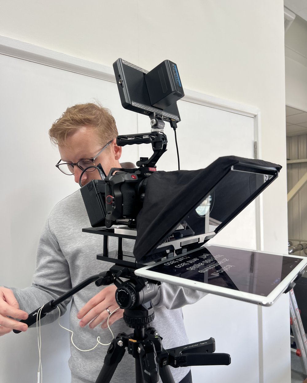 Sam threading a cable on a camera and teleprompter rig before a scripted shoot
