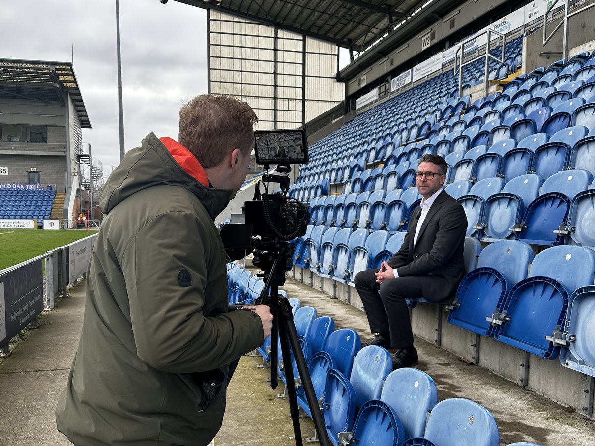 Sam sets the shot at a camera on a tripod while the client sits in the stadium seats ready for a case study interview