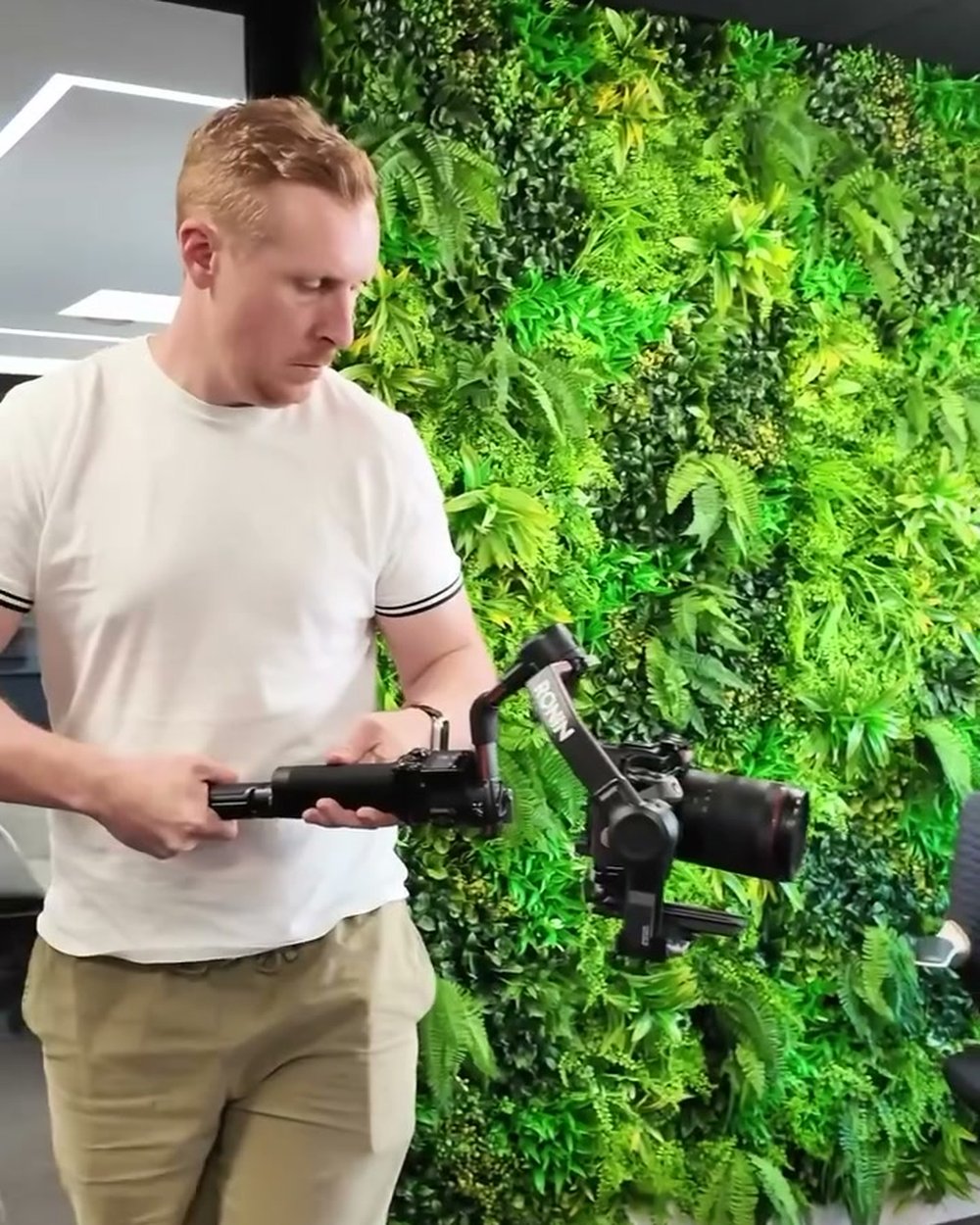 Sam steadying a camera on a gimbal in front of a living green wall