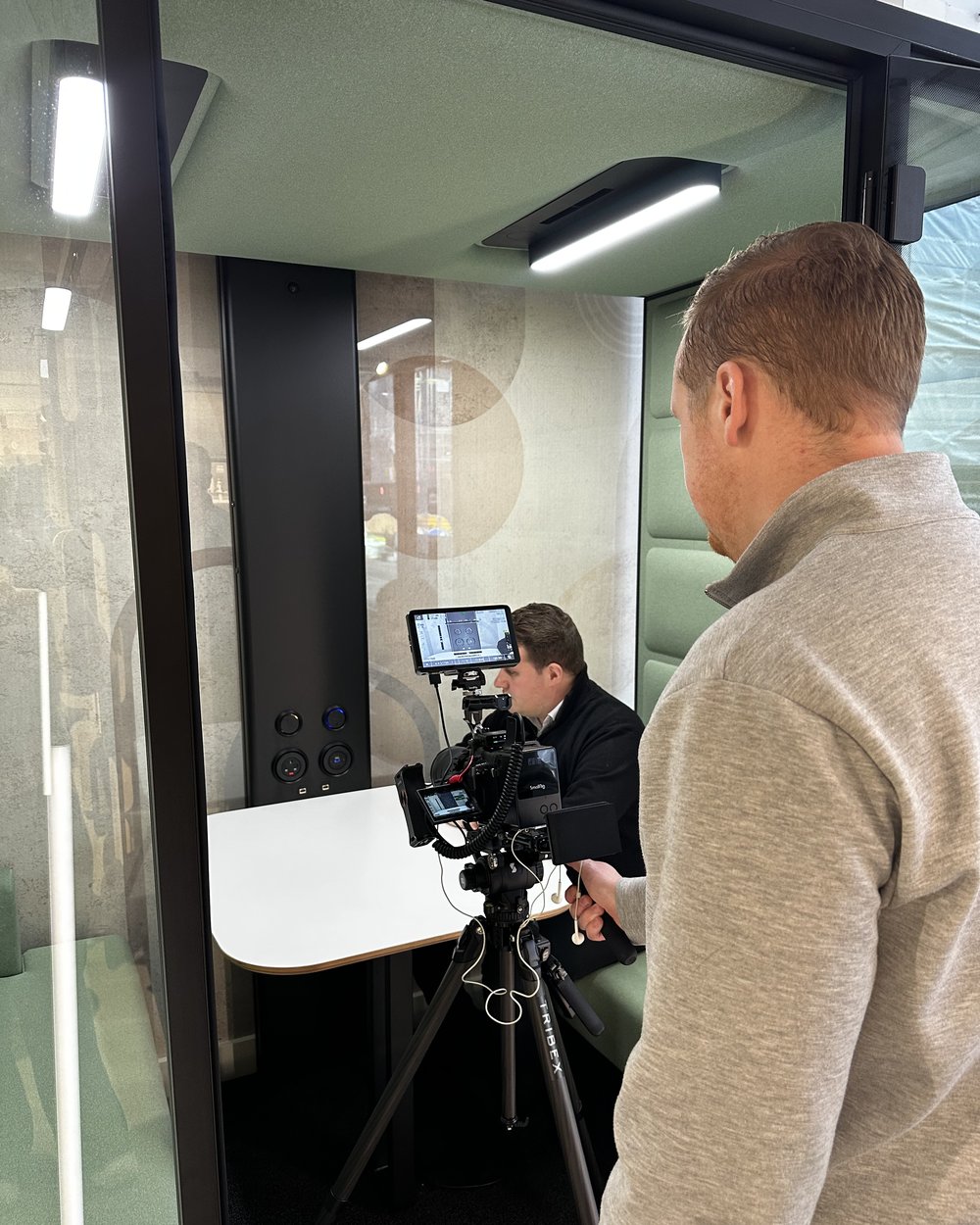 Sam checking the camera monitor on a tripod while the subject sits in a glass pod