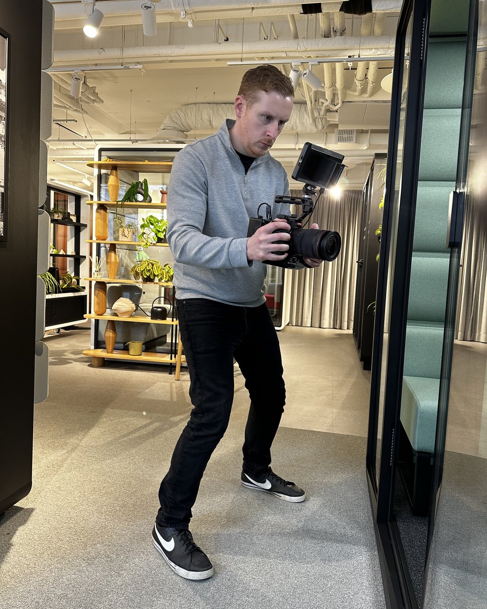 Sam in a low stance with a handheld camera rig framing a shot in a showroom aisle
