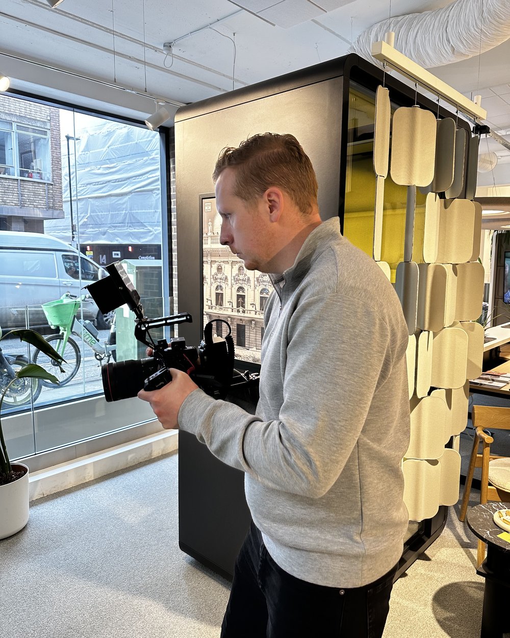 Sam walking a handheld camera rig past a window in a bright building