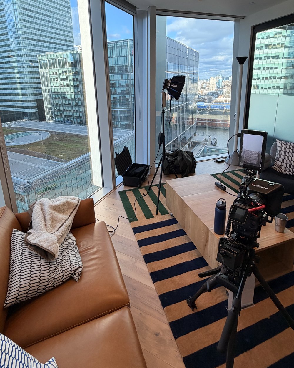 Interview set with a key light on a stand, cinema camera and monitor, a sofa and city skyline windows