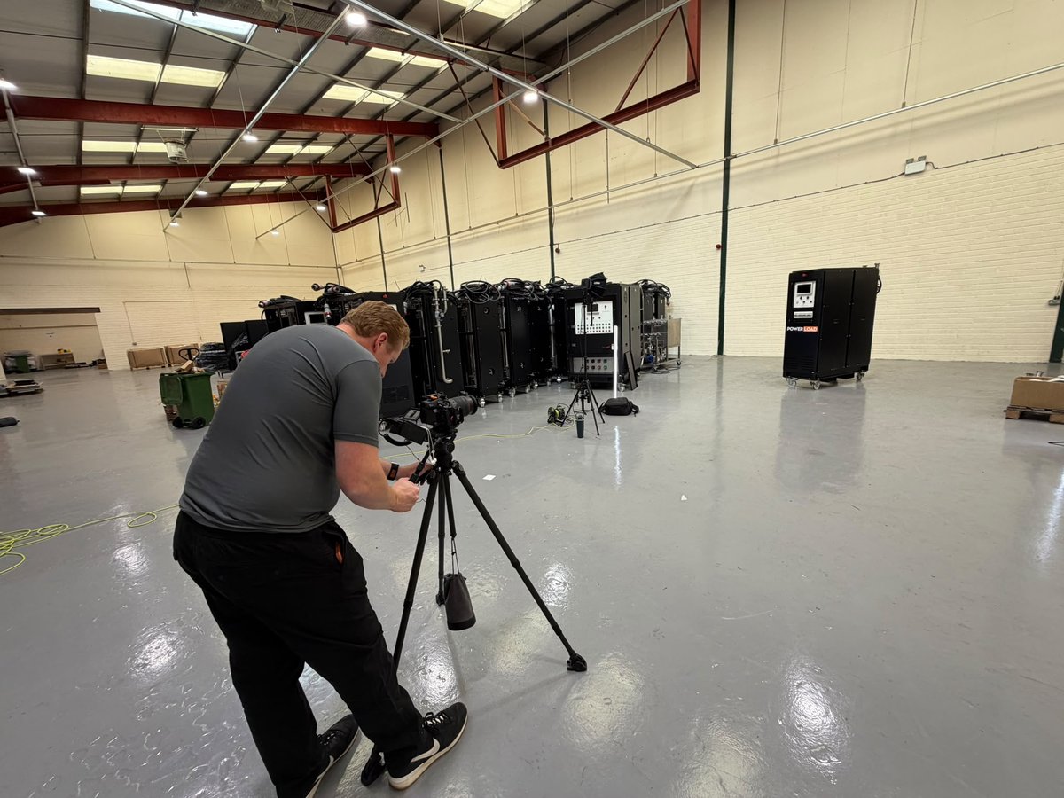 Sam bent over a tripod camera on a factory floor with PowerLoad units lined up behind