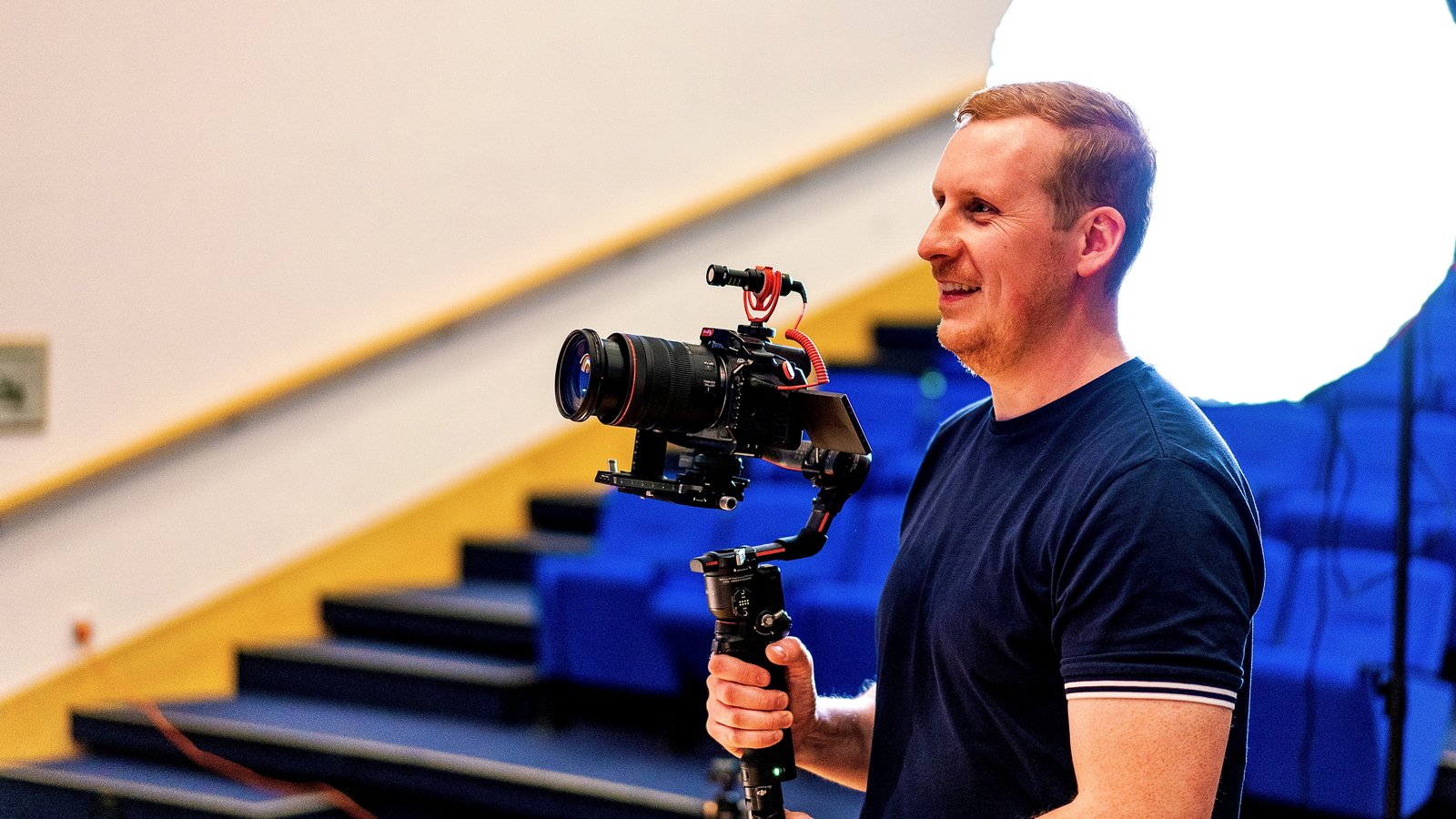 Sam laughing with a gimbal camera in front of a softbox and theatre seating