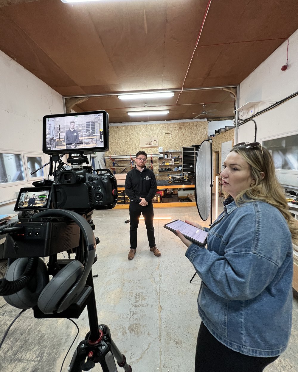 A producer checking a tablet beside a camera and monitor while briefing a presenter in a workshop
