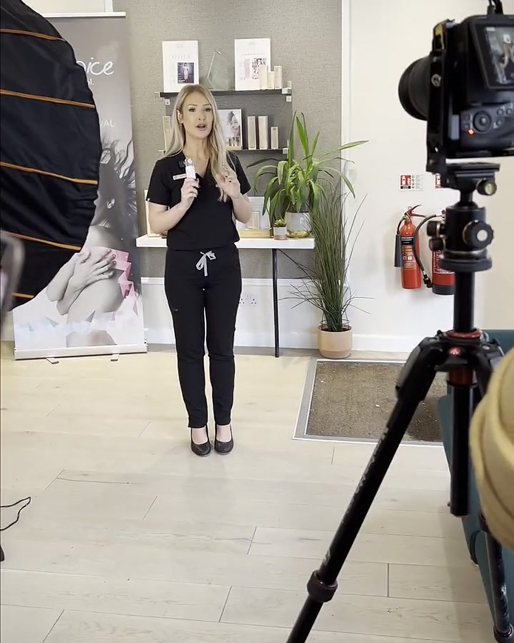 A therapist presenting to camera in a clinic reception, with our camera on a tripod and a softbox beside it