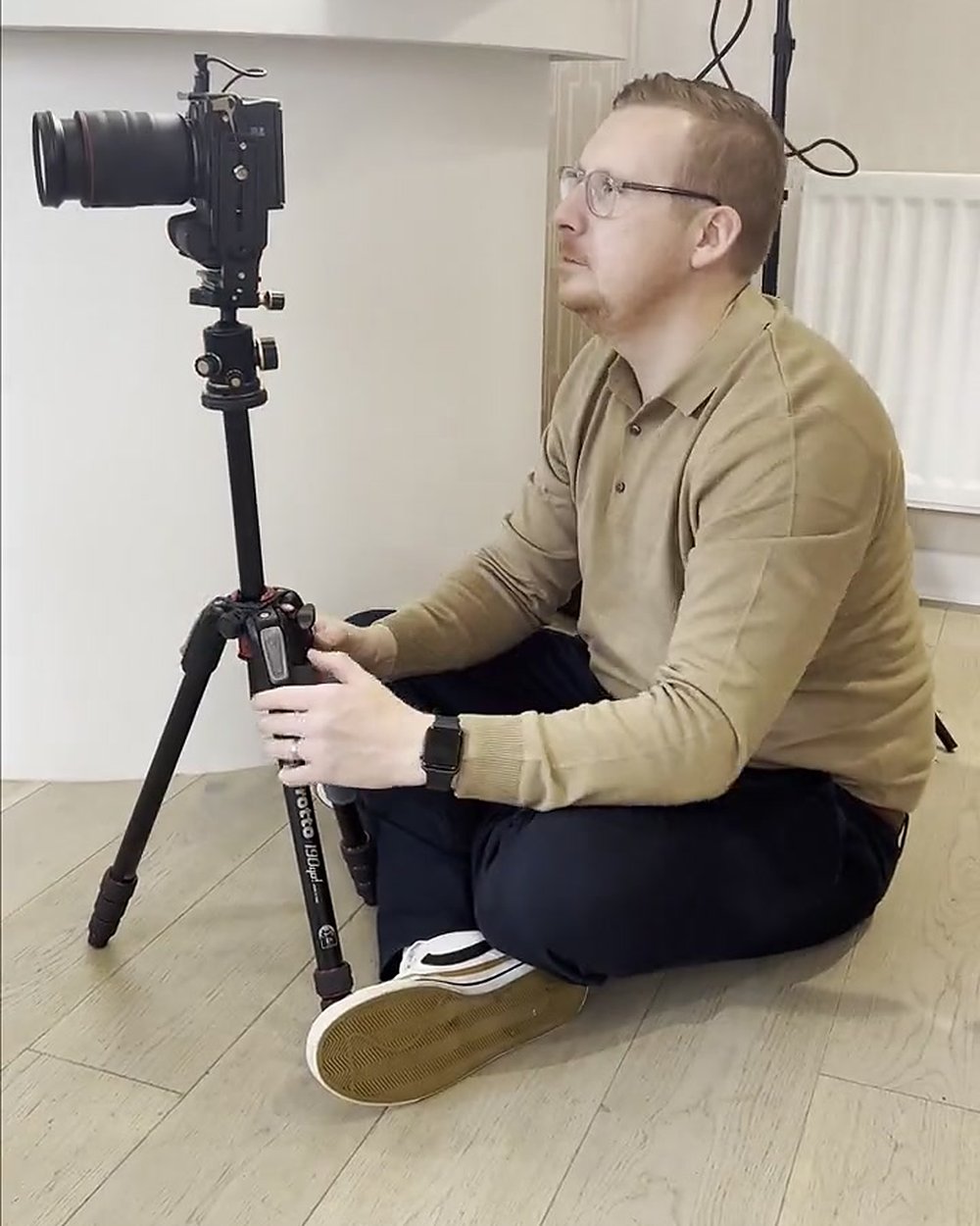 Sam sitting on the floor of a beauty clinic holding a tripod with a camera on a content day