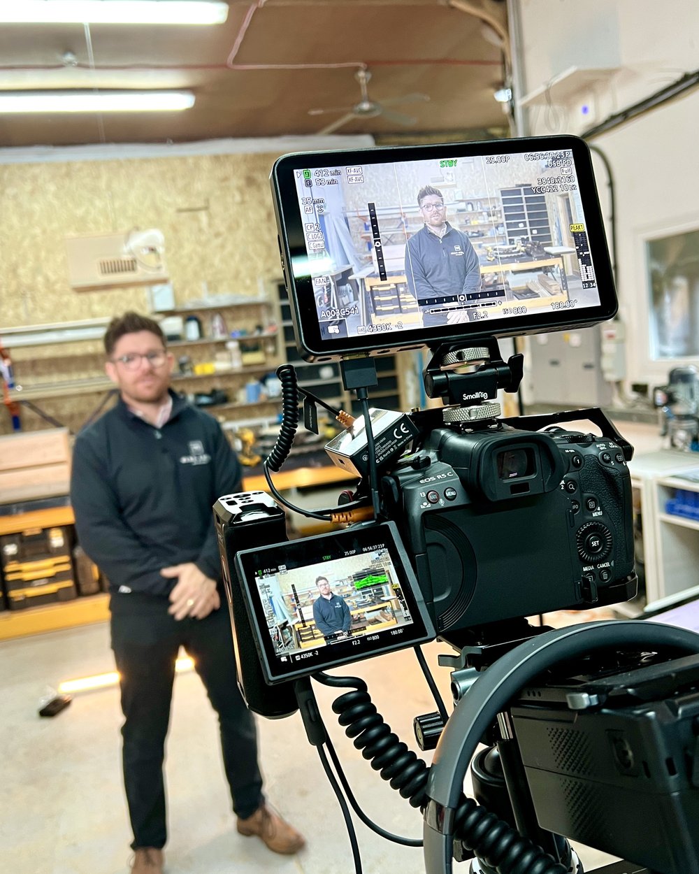 A presenter standing to camera in a joinery workshop, with our camera and two monitors in the foreground