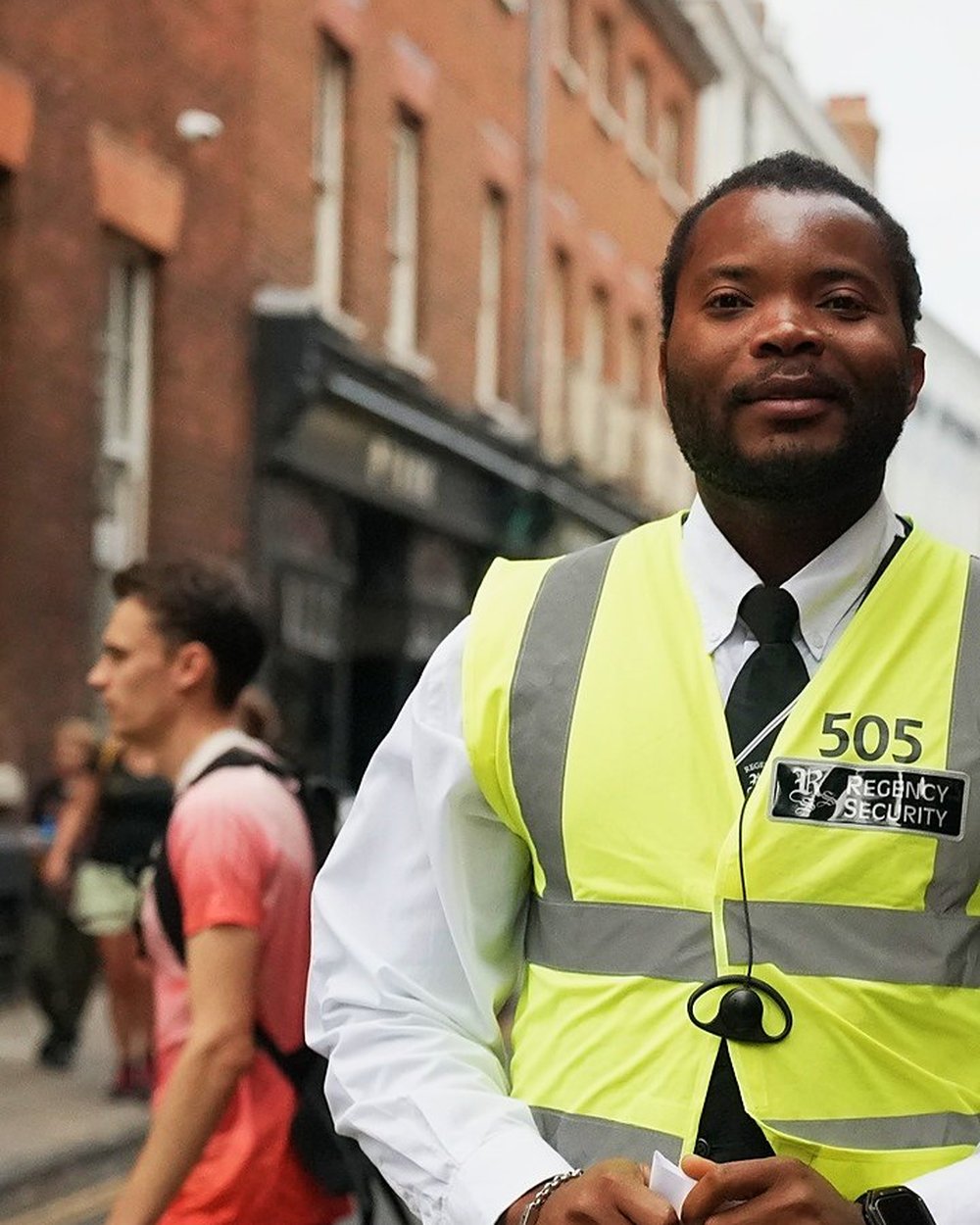 A Regency Security officer in a hi-vis vest on a Norwich street during Run Norwich, with runners and spectators behind