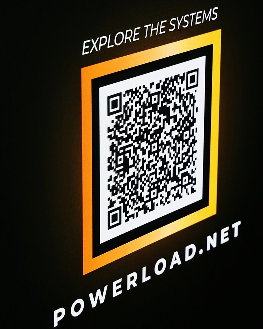 A glowing orange QR code panel on a stand screen reading Explore the systems