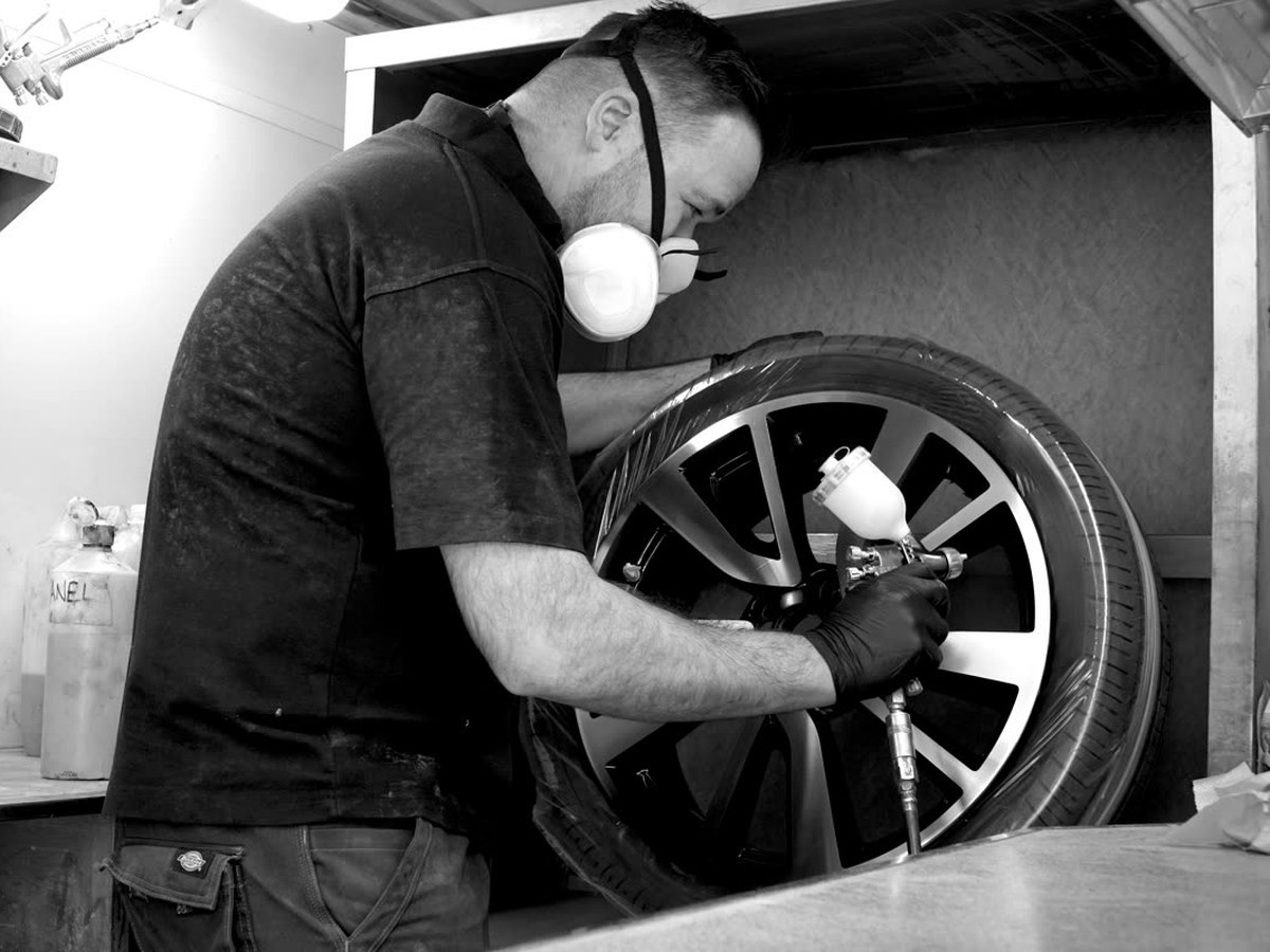A technician in a mask spraying an alloy wheel in the booth