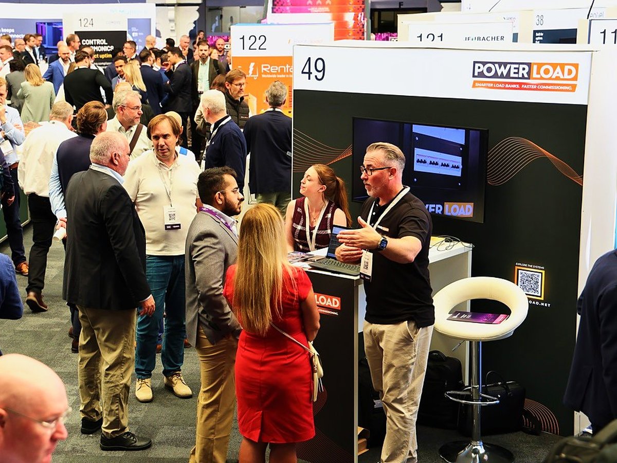 A busy PowerLoad exhibition stand at Data Centre World with visitors and a presenter